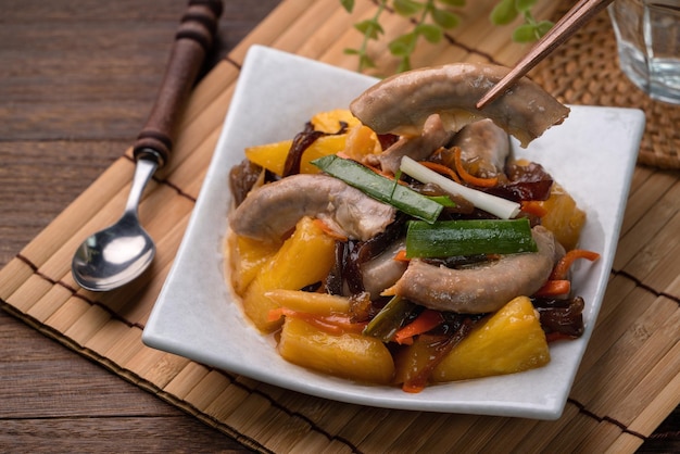 Comer intestino delgado de cerdo frito con piña. Deliciosa comida casera con hongo negro y cebolleta sobre fondo de mesa de madera.