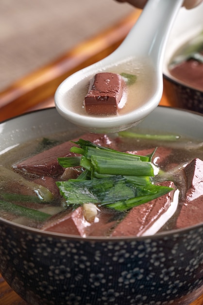 Comer sopa de sangre de cerdo, comida tradicional taiwanesa casera con hojas de mostaza en escabeche y brotes de ajo en un recipiente sobre la mesa de madera.