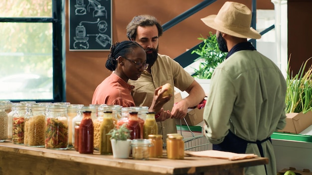 Un comerciante asiste a los clientes en una tienda de comestibles mostrando frutas y verduras recién cosechadas Una pareja joven en busca de productos orgánicos en un supermercado local de cero residuos estilo de vida sostenible