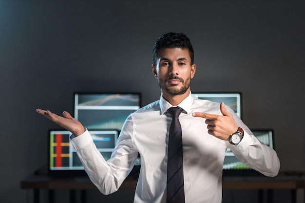 Comerciante birracial señalando con el dedo y computadoras con gráficos en el fondo