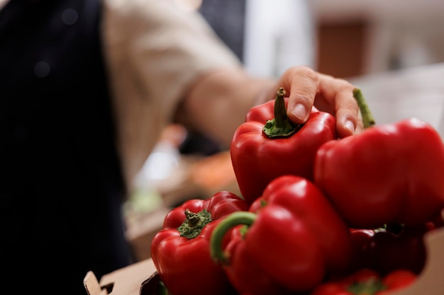 Comerciante llenando cajas en los estantes de las tiendas sin desperdicio con pimientos rojos de cosecha propia de su propio jardín. Tendero reabasteciendo la tienda local del vecindario con alimentos ecológicos, de cerca