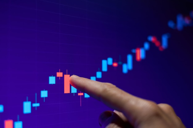 El comerciante señala con el dedo el gráfico de acciones en aumento en el monitor