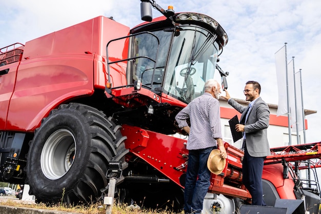 Foto comerciante de tractores presentando una nueva cosechadora al agricultor