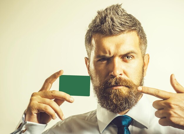 El comercio electrónico y la banca, el éxito financiero, el concepto de compras en línea: un hombre casual elegante atractivo con camisa y corbata muestra el dedo en una tarjeta de presentación en blanco o una tarjeta de crédito plástica. Copie el espacio para hacer publicidad.