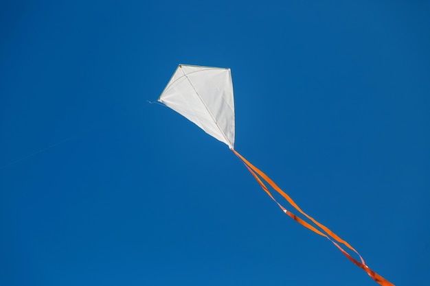 Foto cometa de cola roja blanca volando contra el cielo azul claro.