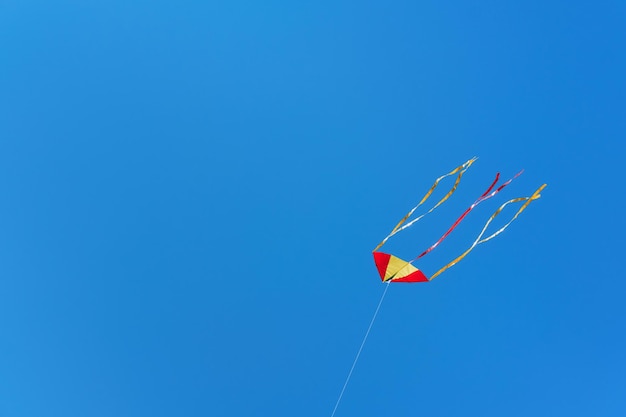 Foto la cometa roja y amarilla vuela alto en el cielo azul sin nubes espacio de copia de enfoque suave