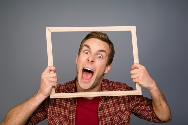 Comic joven mostrando la lengua y sosteniendo el marco de madera