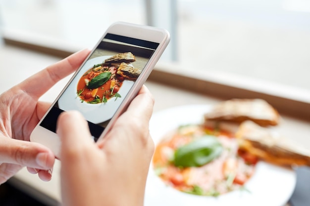 comida, alimentação, tecnologia, culinária e conceito de pessoas - mãos de mulher com sopa de gazpacho foto na tela do smartphone em um restaurante