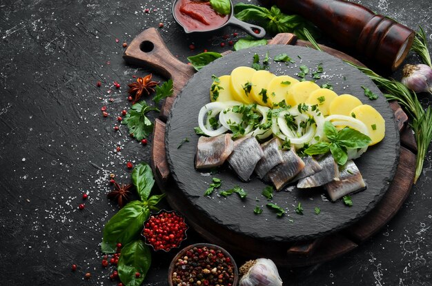 Comida Arenque con cebollas y patatas en un plato de piedra negra Vista superior Espacio libre para el texto