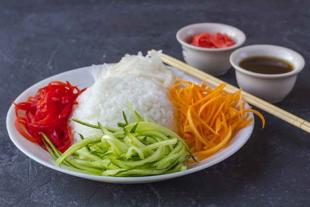 Comida asiática: arroz blanco y verduras (zanahorias, pepinos, daikon) en un primer plano oscuro.