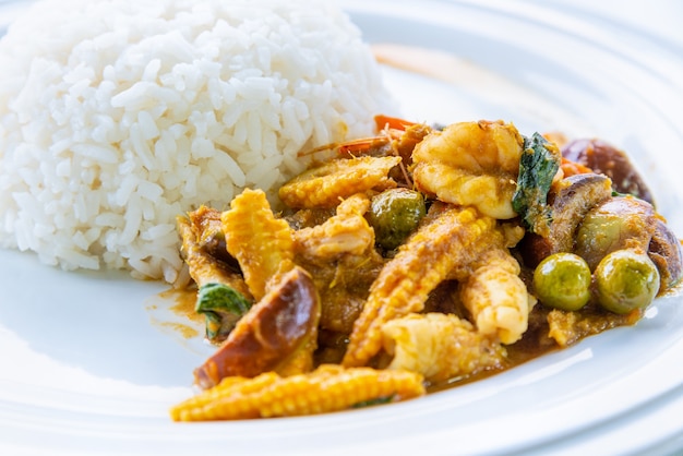 Comida asiática picante quente ou comida tailandesa, vista lateral do close up acima Camarão verde curry baby Milho e leite de coco frito com arroz branco cozido em um fundo de prato branco redondo limpo para cozinhar refeições deliciosas