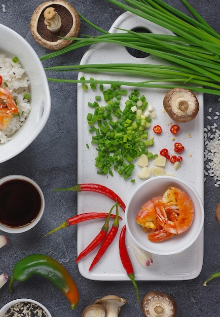 Comida asiática sobre fundo escuro, arroz wok com camarões e cogumelos, durante a preparação, vertical, vista superior