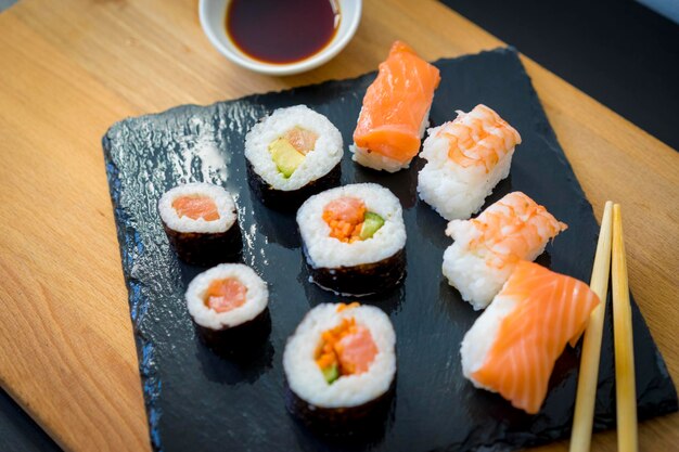 Comida asiática, sushi en una mesa de madera en un plato de pizarra negra con salsa de soja y palillos