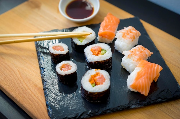 Comida asiática, sushi en una mesa de madera en un plato de pizarra negra con salsa de soja y palillos