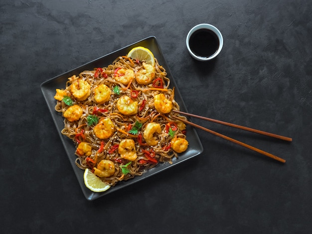 Comida asiática udon fideos con gambas fritas, sésamo y pimienta de cerca en un plato