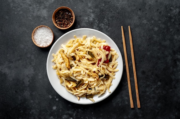 Comida asiática udon fideos con pollo y verduras en un plato blanco sobre un fondo de piedra