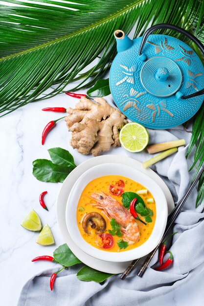 Comida y bebida, cocina tradicional tailandesa. Spicy tom yam kung, sopa agria tom yum con camarones, gambas, leche de coco, hierba de limón y ají en un bol sobre una mesa blanca. endecha plana