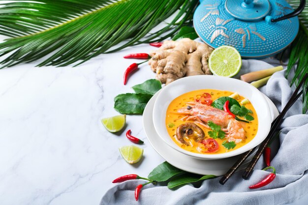 Comida y bebida, cocina tradicional tailandesa. Tom yam kung picante, sopa agria tom yum con camarones, gambas, leche de coco, hierba de limón y ají en un bol sobre una mesa blanca