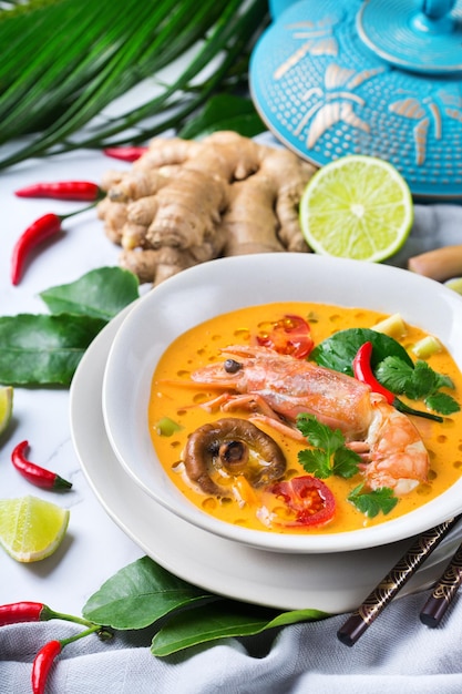 Comida y bebida, cocina tradicional tailandesa. Tom yam kung picante, sopa agria tom yum con camarones, gambas, leche de coco, hierba de limón y ají en un bol sobre una mesa blanca