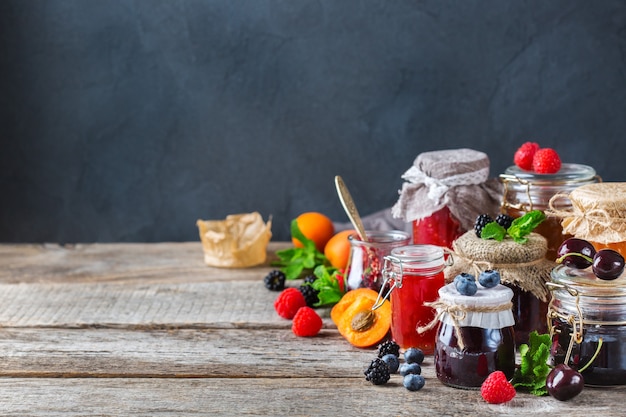 Comida y bebida, concepto de cosecha verano otoño. Surtido de mermeladas de frutas y bayas de temporada en frascos sobre una mesa de madera. Copia espacio fondo rústico