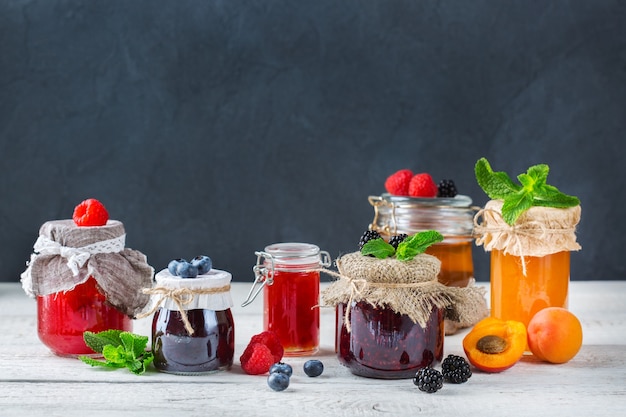 Comida y bebida, concepto de cosecha verano otoño. Surtido de mermeladas de frutas y bayas de temporada en frascos sobre una mesa de madera. Copia espacio fondo rústico