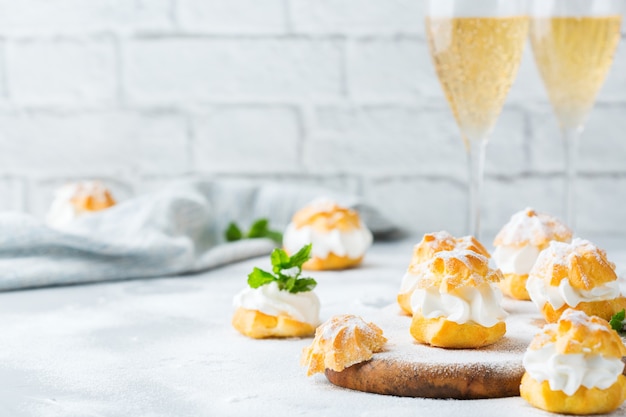 Comida y bebida, concepto de vacaciones. Profiteroles caseros dulces deliciosos con crema y vasos de champán en una mesa de cocina moderna