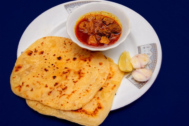 Foto comida bengalí carne de vacuno con paratha sobre fondo azul.