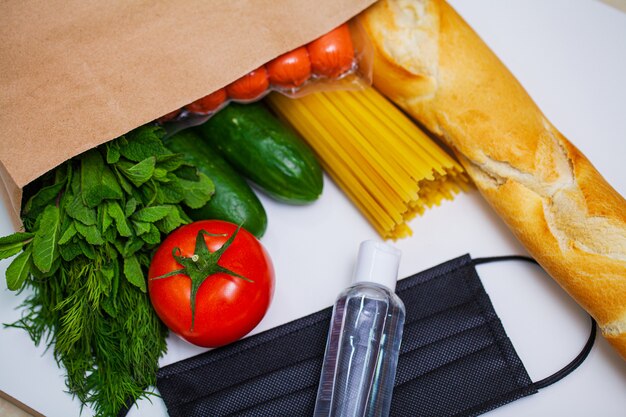 Comida en bolsa de papel con mascarilla médica y botella de gel