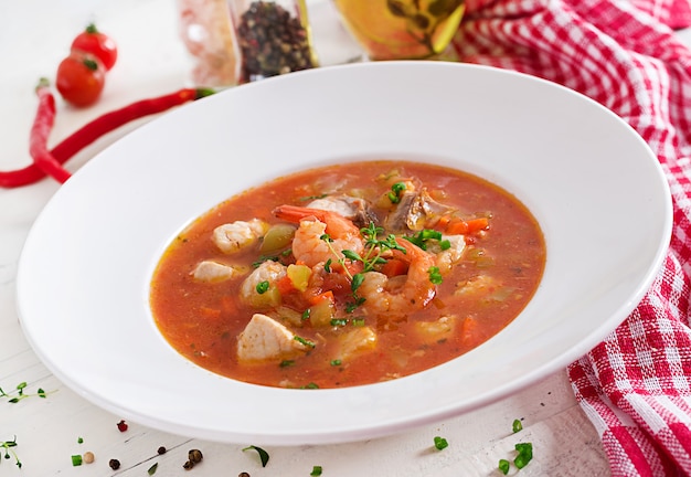 Foto comida brasileña: moqueca capixaba de pescado y pimientos en salsa de coco picante en un plato sobre una mesa de madera blanca. estofado de pescado brasileño.