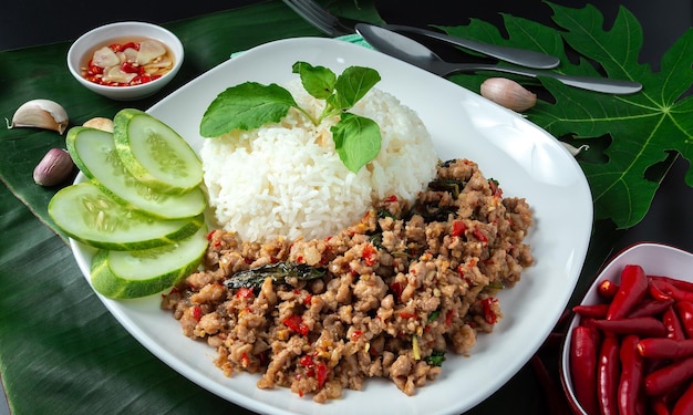 Comida callejera tailandesa albahaca arroz frito cerdo picado huevo frito y rodajas de pepino en una mesa negra