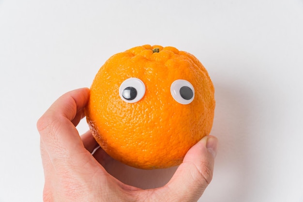 Comida con caras divertidas Mandarín con ojos Mano sujetando el carácter de mandarina sobre fondo blanco