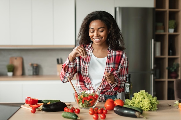 Comida casera y cuidado de la salud Alegre joven chef negra en ensalada casual de sales de verduras orgánicas