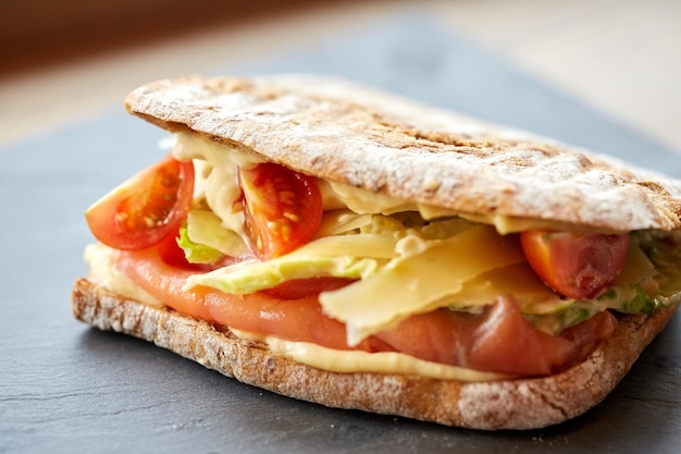 comida, cena y concepto de comida - sándwich de panini de salmón con tomates y queso en un plato de piedra en el restaurante