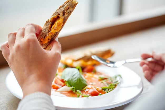 Foto comida, cena, culinaria y concepto de personas - primer plano de una mujer comiendo sopa de gazpacho con sándwich y cuchara en un restaurante