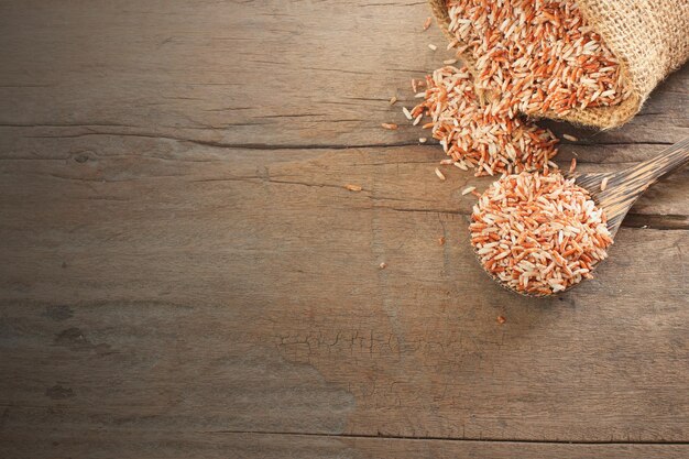 Foto comida de cereales tailandesa vista superior del arroz integral rojo orgánico en una cuchara de madera y un saco sobre una mesa de madera con espacio para copiar