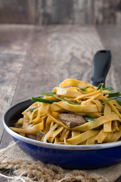 Comida china chow mein de carne en sartén sobre mesa de madera