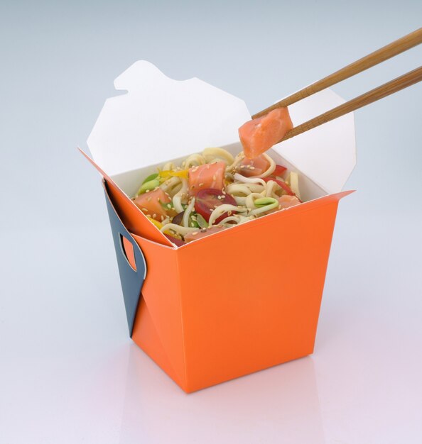 Comida china para llevar Fideos con carne y verduras en una caja de cartón sobre un fondo claro