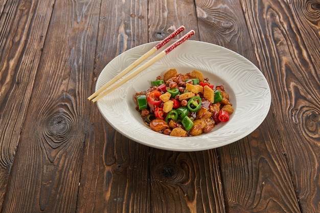 Comida china, pollo kung pao en plato blanco con palillos en la mesa de madera, vista superior y espacio de copia