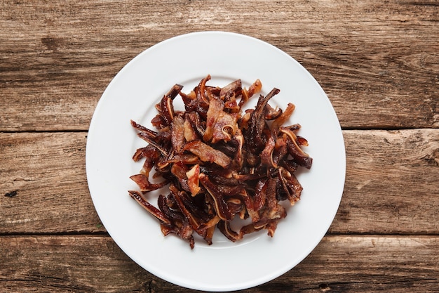 Comida chinesa, petiscos saborosos de cerveja. Orelhas de porco picantes fumadas servidas no prato branco, mesa de madeira rústica. Vista do topo.