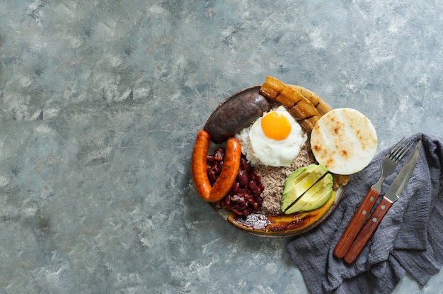 Comida colombiana Bandeja paisa, plato típico de la región de Antioquia en Colombia: panceta de cerdo frita, morcilla, salchicha, arepa, frijoles, plátano frito, huevo de aguacate y arroz.