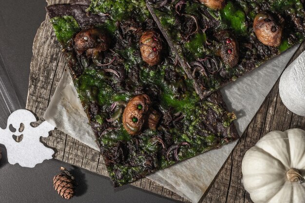 Comida de concepto de Halloween. Pan plano o pizza con tinta de calamar, queso verde, champiñones y cebolla morada. Pan de Muerto con decoración festiva, calabaza blanca, velas y telaraña. Fondo de piedra oscura