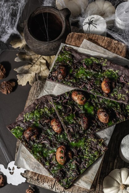 Comida de concepto de Halloween. Pan plano o pizza con tinta de calamar, queso verde, champiñones y cebolla morada. Pan de Muerto con decoración festiva, calabaza blanca, velas y telaraña. Fondo de piedra oscura