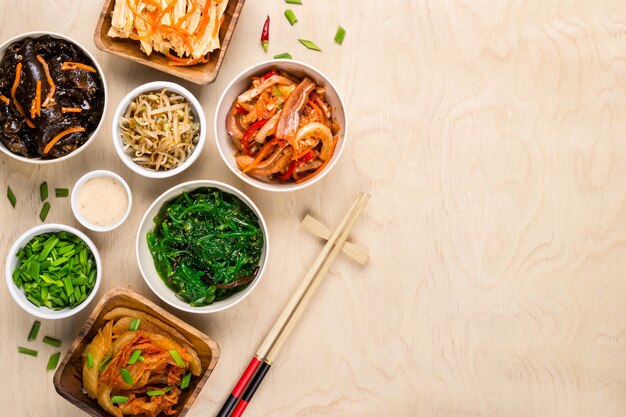 Comida coreana variada e pauzinhos em fundo de madeira.