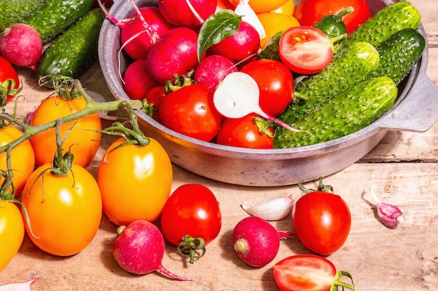 Comida, cosecha, concepto de verano. Surtido de tomates maduros orgánicos rojos y amarillos, pepinos, rábanos, ajo y hojas frescas de albahaca. Mesa de madera antigua, lugar para texto