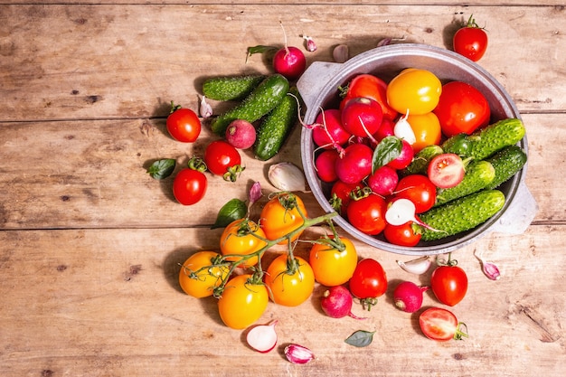 Comida, cosecha, concepto de verano. Surtido de tomates maduros orgánicos rojos y amarillos, pepinos, rábanos, ajo y hojas frescas de albahaca. Mesa de madera vieja, vista superior