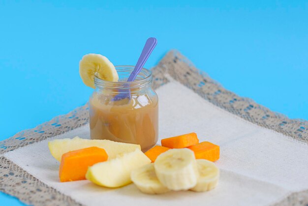 Comida de bebê artesanal de frutas com maçãs, bananas, peras e abóbora em potes de vidro em um fundo azul, copie alimentos saudáveis para crianças