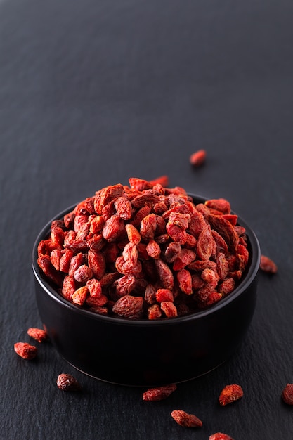 Comida de cérebro super seca goji berry em copo cerâmico preto na placa de pedra ardósia