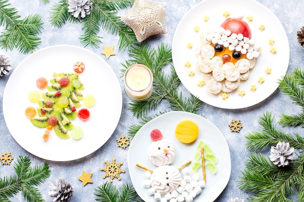 Comida de Natal para crianças - árvore de Natal de kiwi, boneco de neve de marshmallow, banana, Papai Noel. Vista do topo