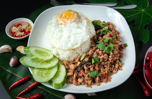 Comida de rua tailandesa manjericão arroz frito carne de porco picada ovo frito e pepino fatiado em uma mesa preta