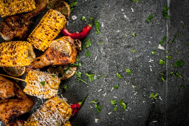 Comida de verão. ideias para churrasco, festa de churrasco. milho e frango (pernas, asas) grelhados, fritos em fogo. com uma pitada de queijo (elotes), pimenta quente, limão. mesa de pedra escura. vista superior do espaço da cópia